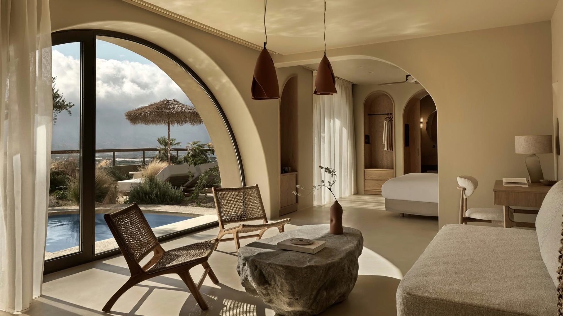 Mediterranean interior with arched window, rattan chairs, and stone coffee table overlooking a pool